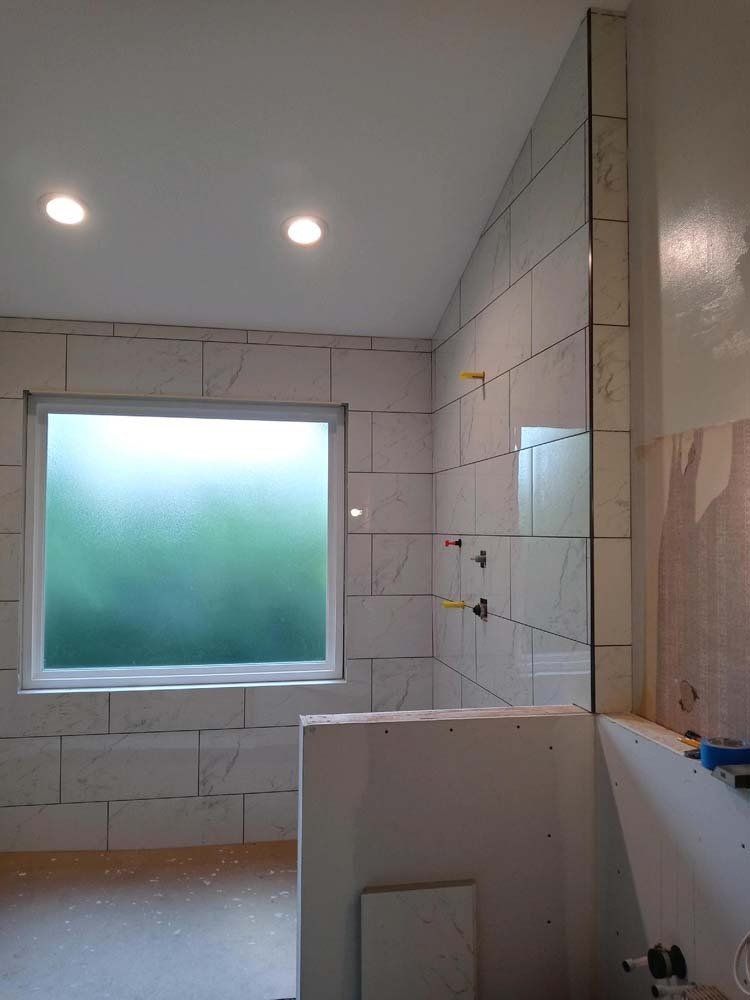 Bathroom shower under construction; white tile, frosted window, glass panel.