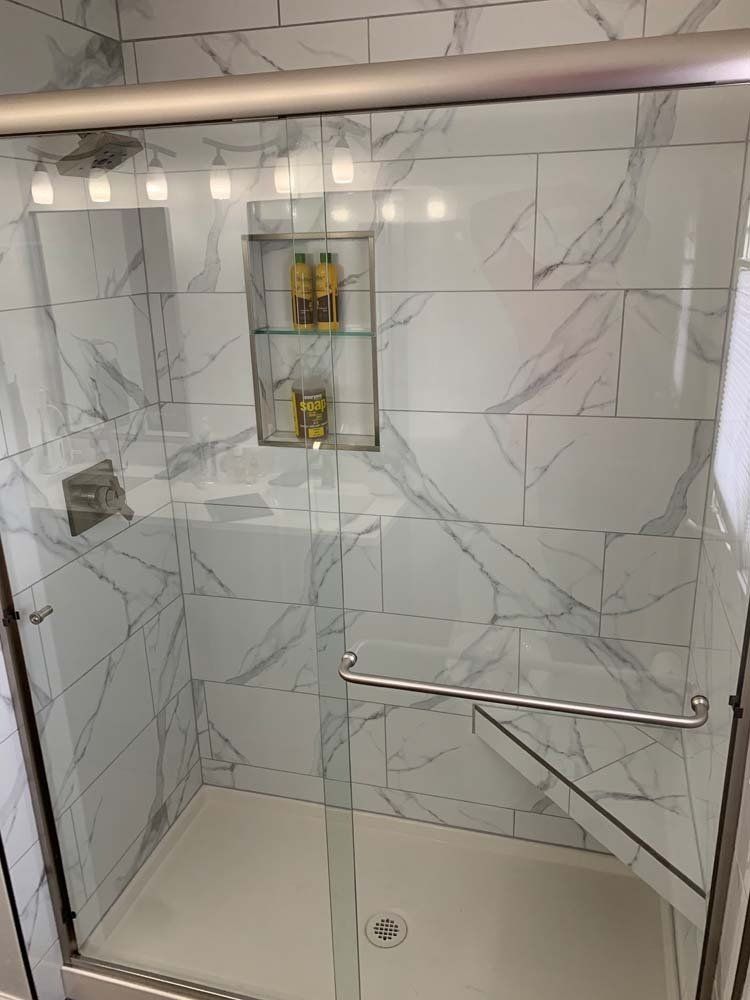 Modern bathroom shower with marble-look tiles, glass door, built-in shelf, and chrome fixtures.