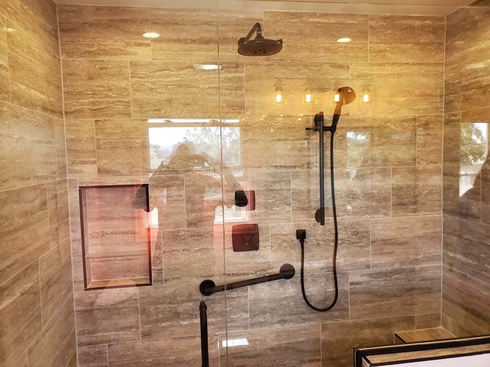 Modern bathroom with tan tile and black shower fixtures, including a handheld showerhead and grab bar.