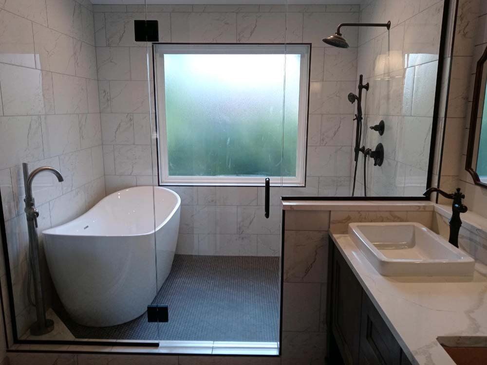 Modern bathroom with freestanding tub, glass shower, and vanity. Gray tile and white fixtures.