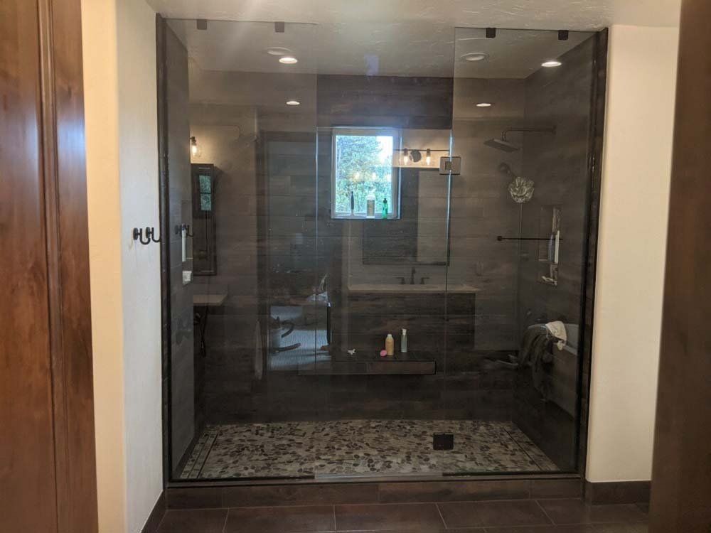 Glass shower enclosure with stone floor and dark brown tiled walls.