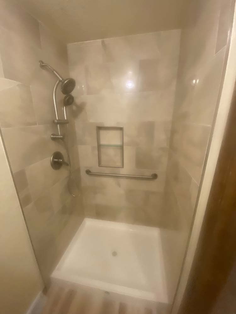 A small shower with beige tile, a white base, grab bar, and shower head.