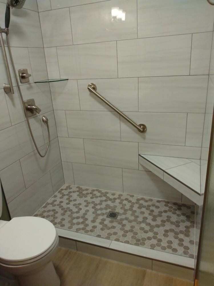 Accessible shower with grab bar, built-in seat, and mosaic tile floor. White walls, chrome fixtures.
