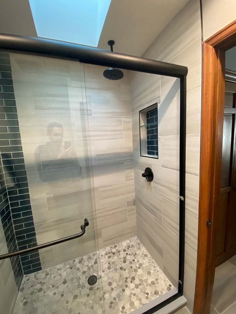 Modern shower with glass door, black fixtures, and stone tile floor.