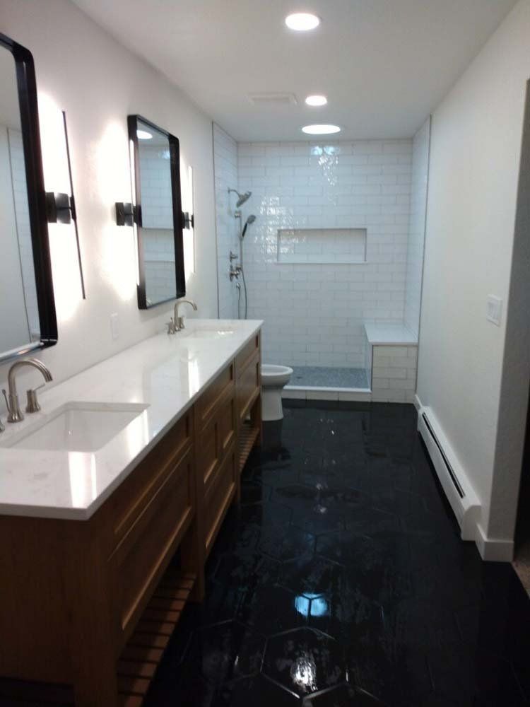 Modern bathroom with black floor, white tiled shower, and a double vanity.