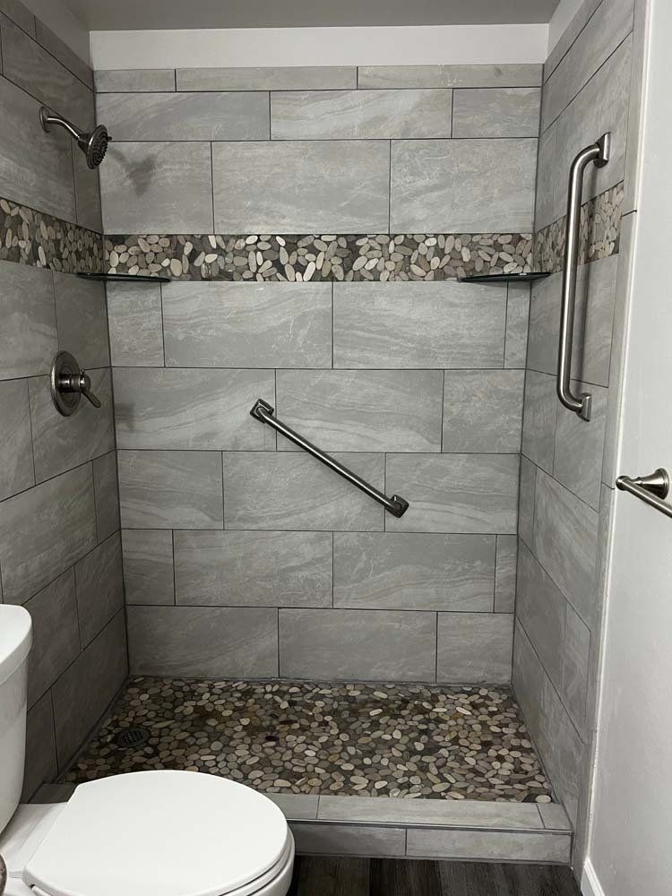 Accessible shower with gray tile, pebble floor, and grab bars.
