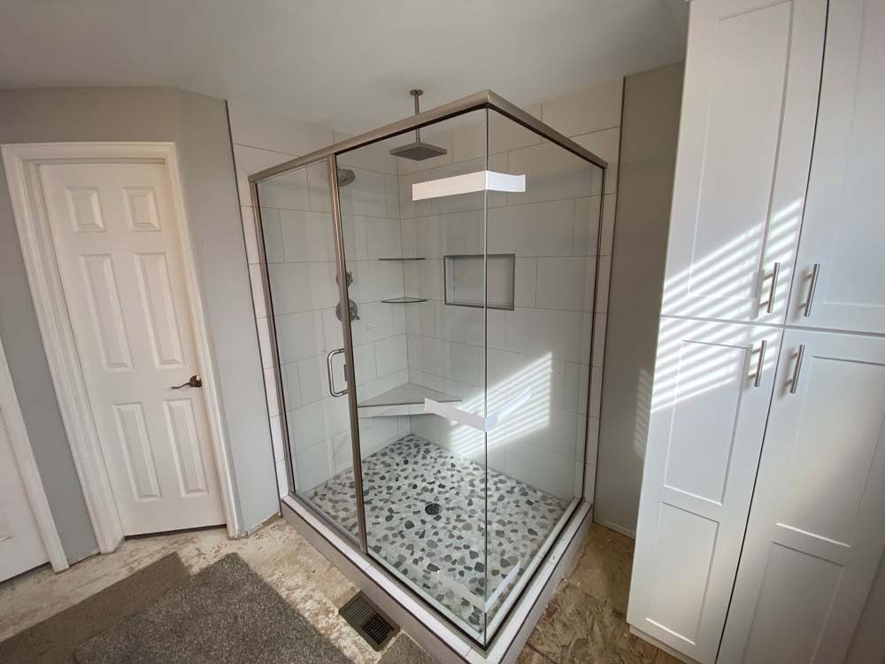 A modern corner shower with glass walls and a tiled floor, adjacent to white cabinets.