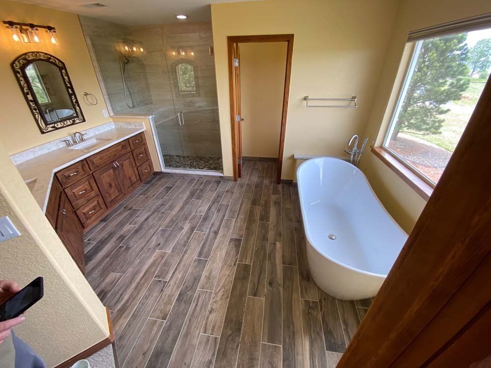 Bathroom with wood-look tile floor, large soaking tub, glass shower, and vanity with mirror.