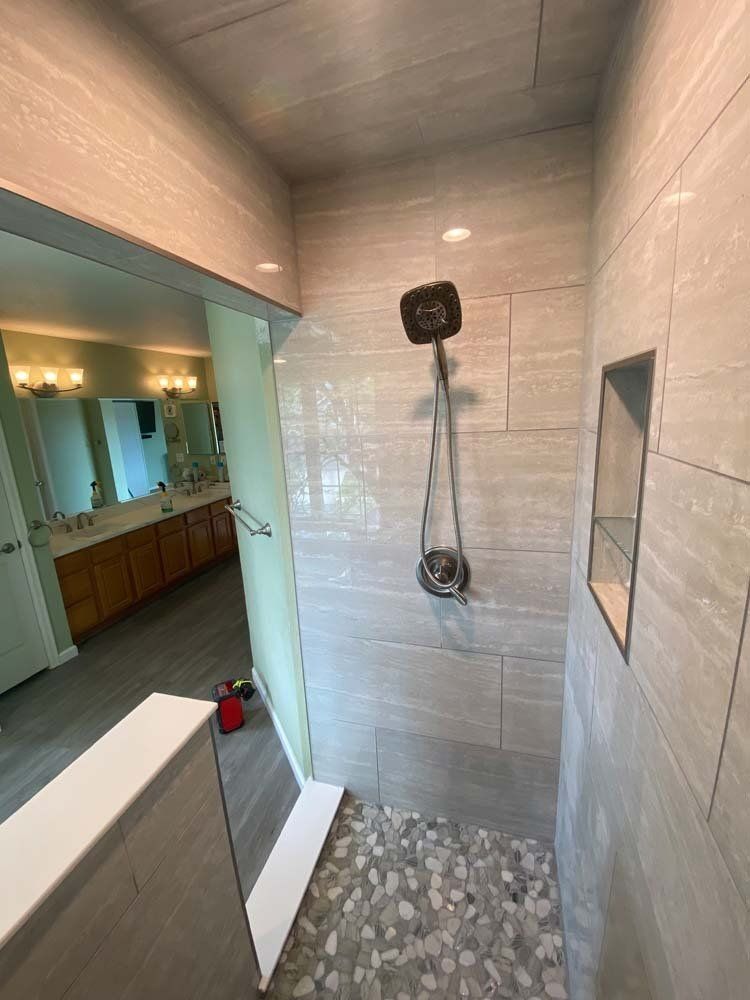 Modern shower with gray tiled walls, pebble floor, and glass door.