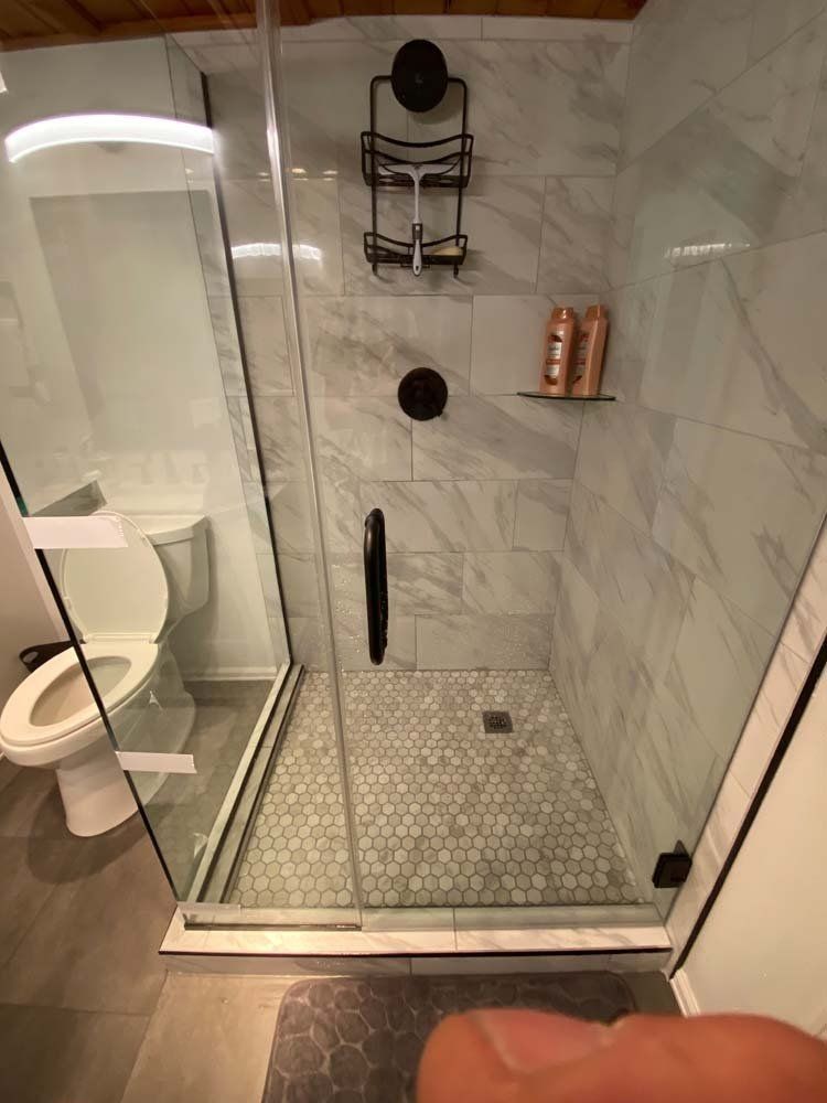 Modern bathroom with a glass shower, toilet, and gray tile walls and floor.