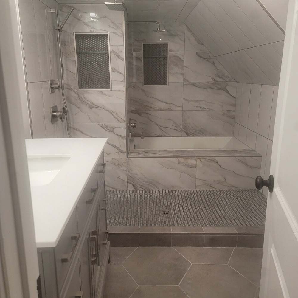 Bathroom with marble-look tile, white vanity, recessed shelving, and a bathtub.