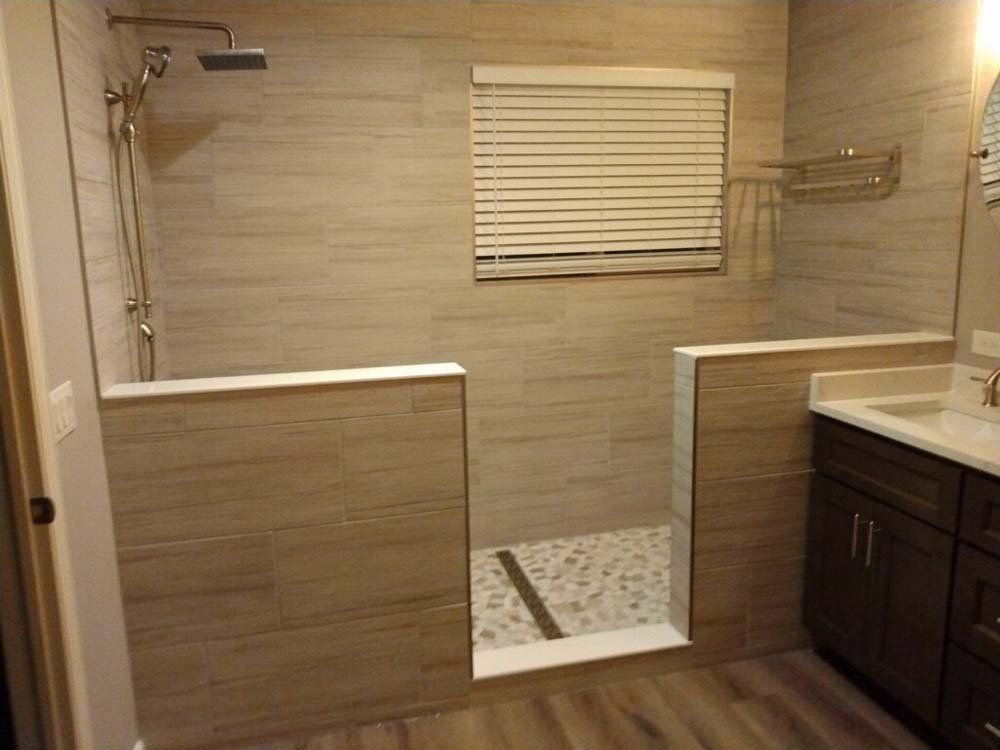 Bathroom with a walk-in shower. Beige tile walls, pebble floor, and a window with blinds.