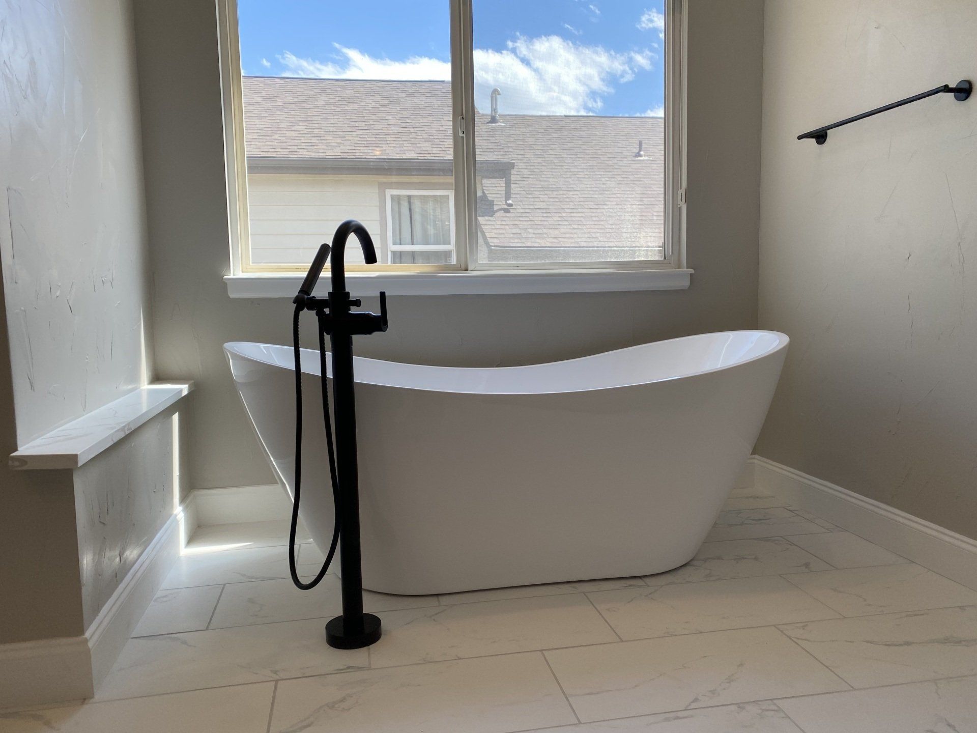 White freestanding bathtub with black faucet, by a window in a bathroom.