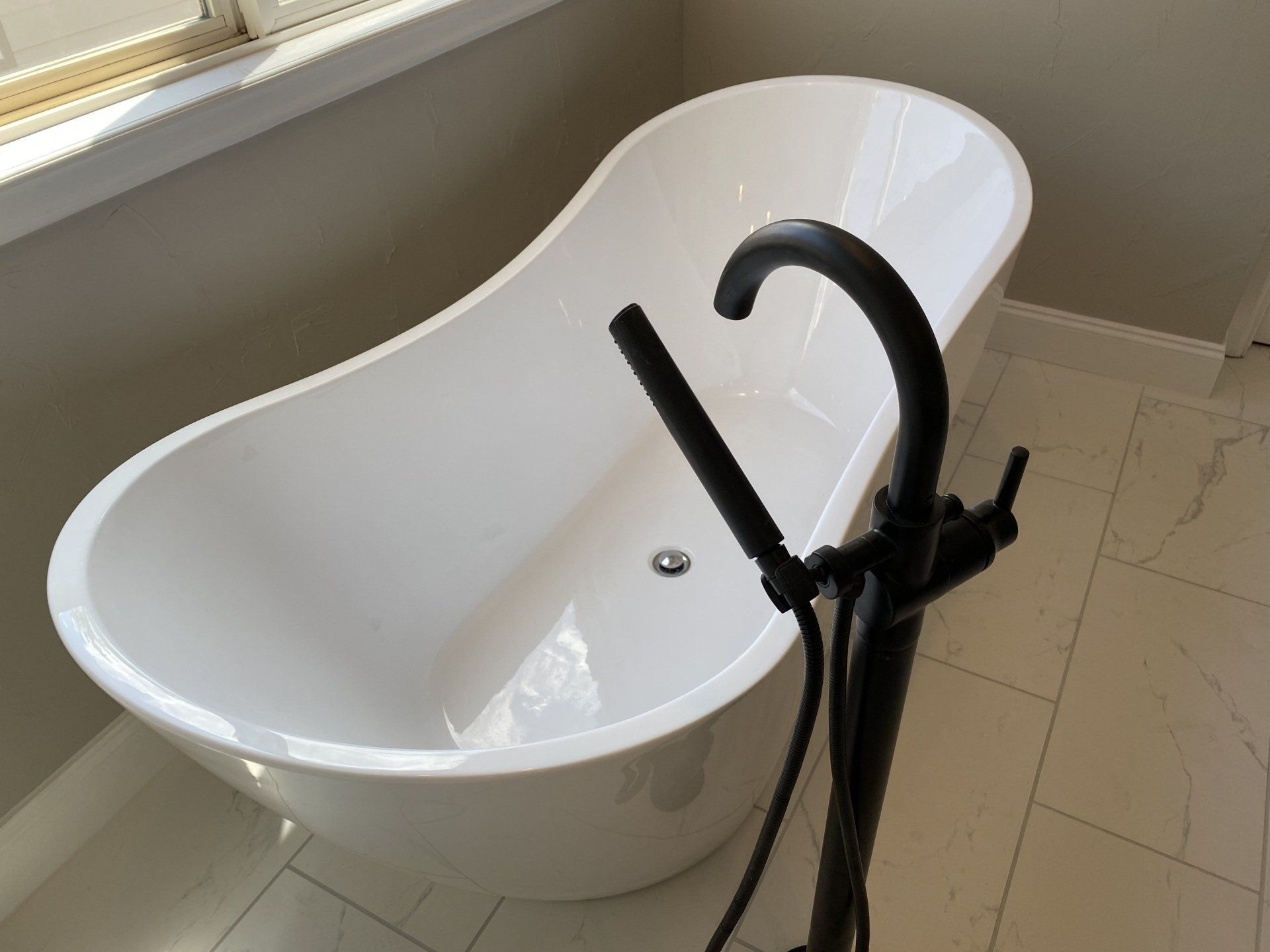 White freestanding bathtub with black faucet in a bathroom, near a window.