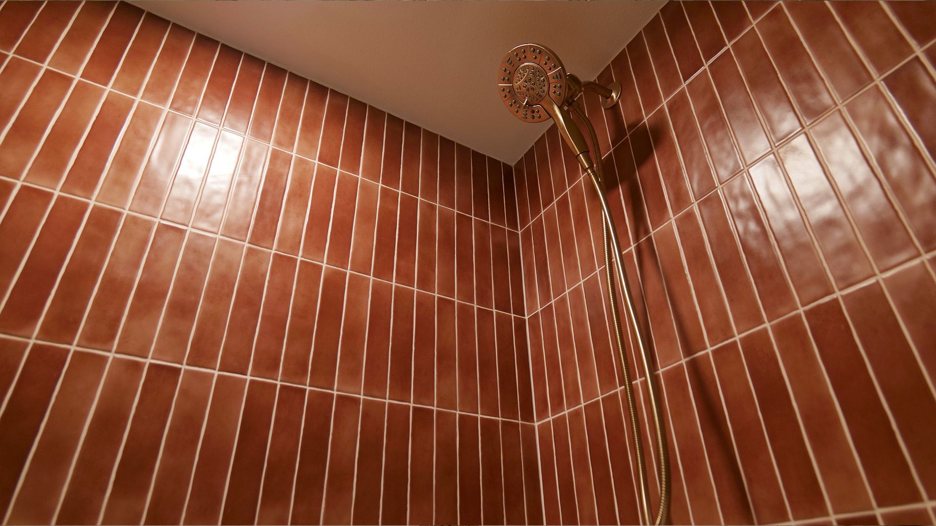 Brown tiled shower with gold showerhead and hose.
