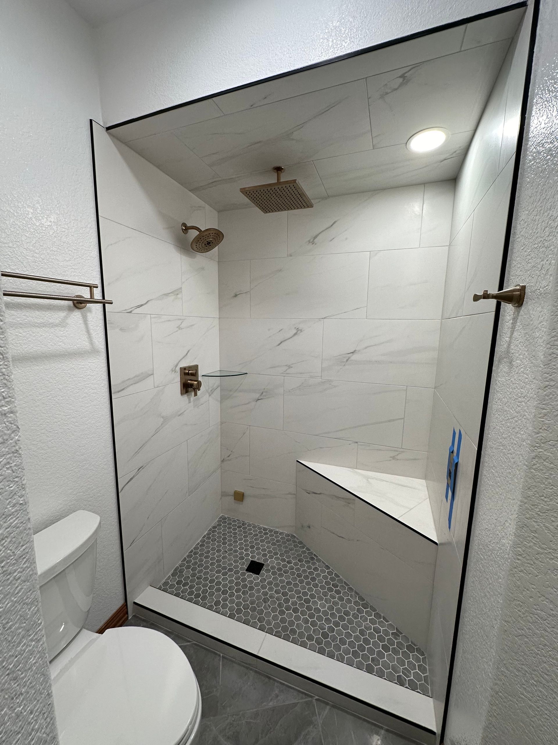 Modern bathroom with marble tile shower, bench, and gray pebble floor. Gold shower fixtures and towel bars.