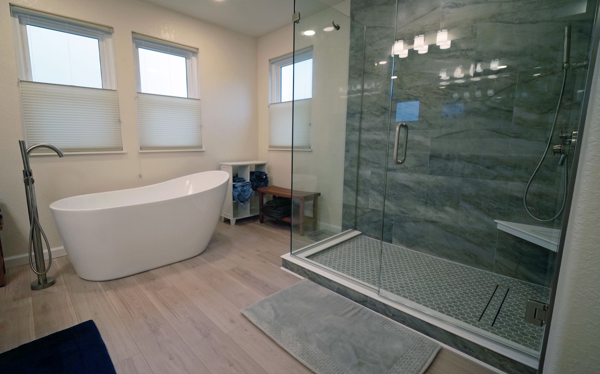 Modern bathroom with white soaking tub, glass shower, light wood floor, and three windows.