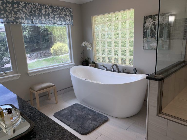 Bathroom with a white freestanding tub, gray rug, and large windows.