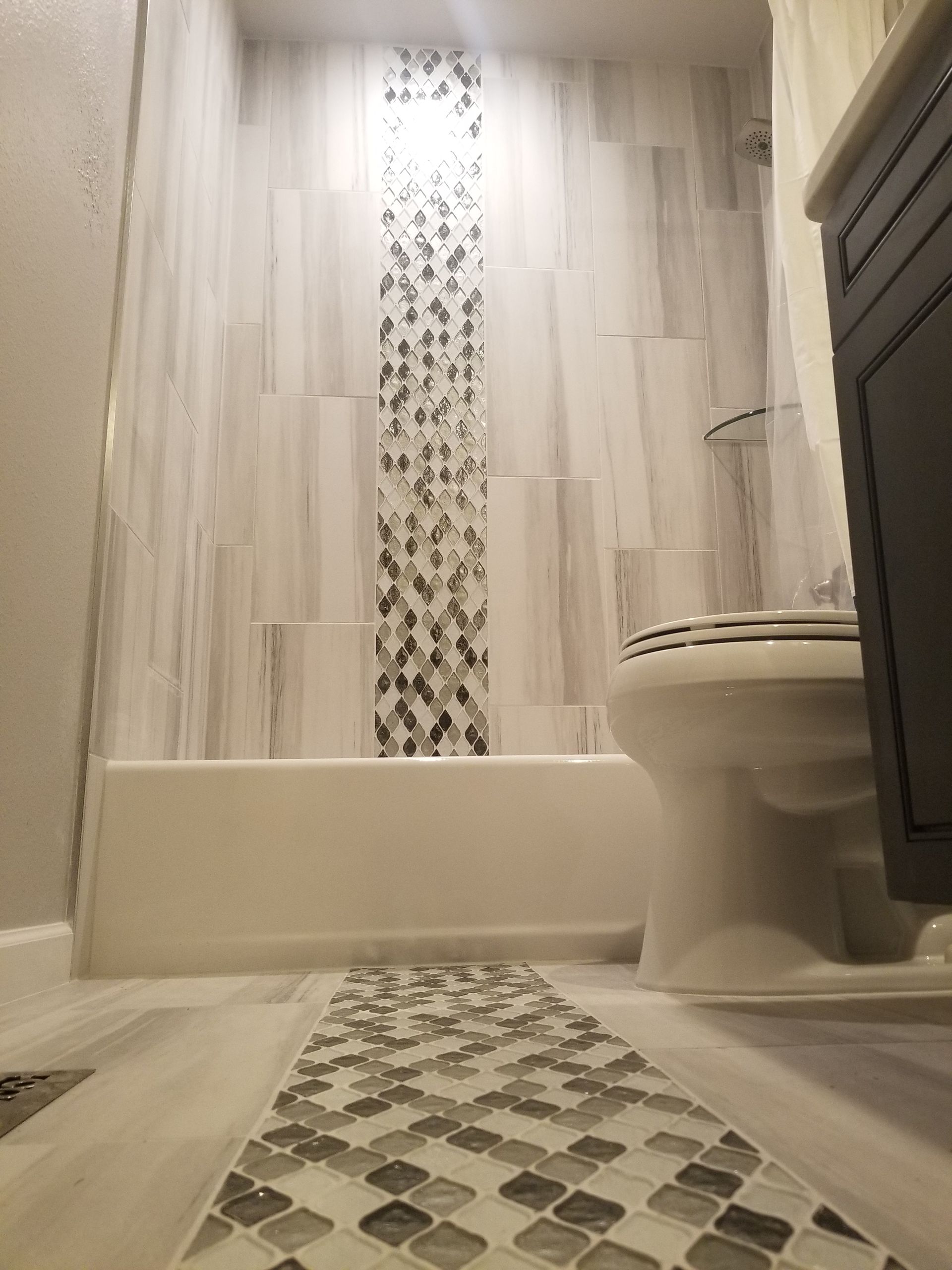 Bathroom with white and gray tiled walls and floor, a white bathtub, and a dark cabinet.