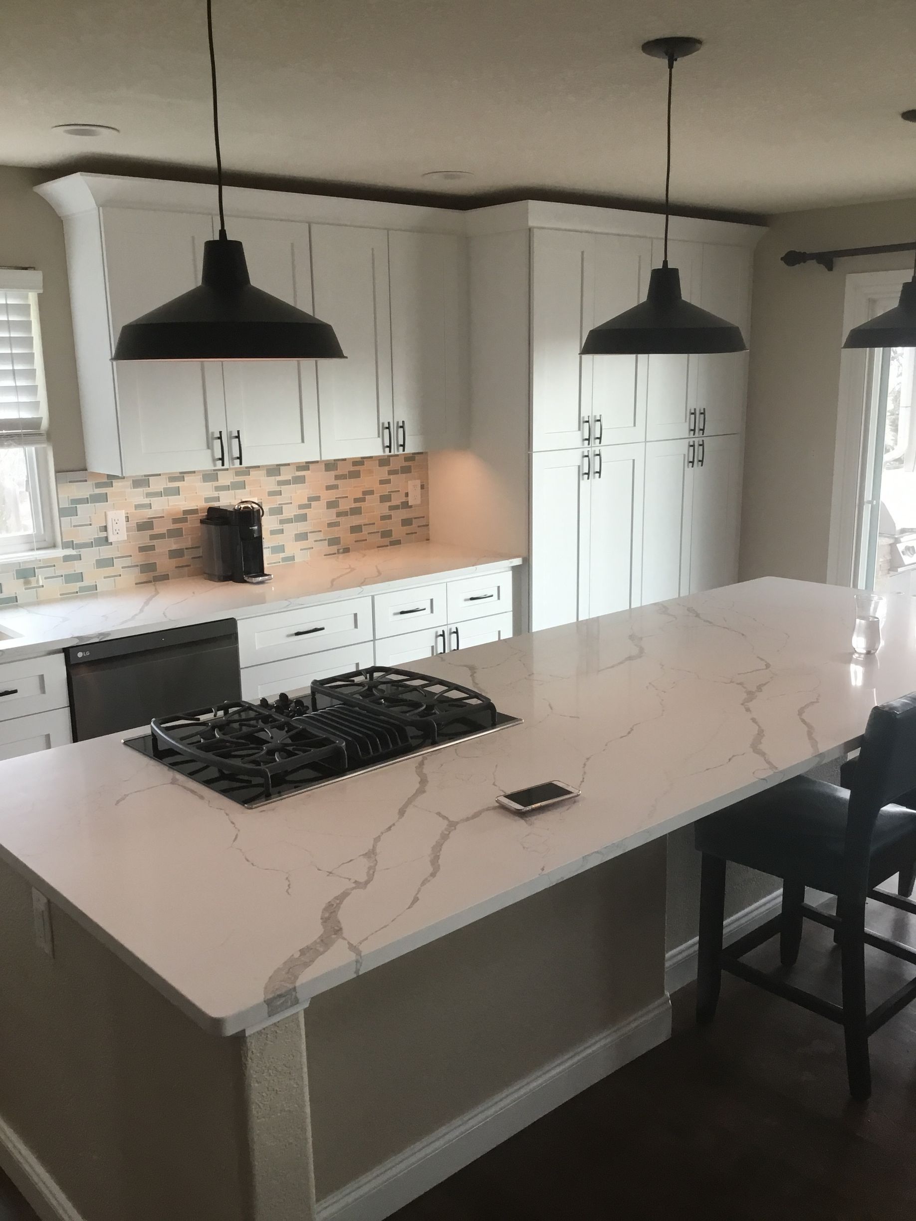 Modern white kitchen with island, quartz countertop, black pendant lights, and gas stovetop.