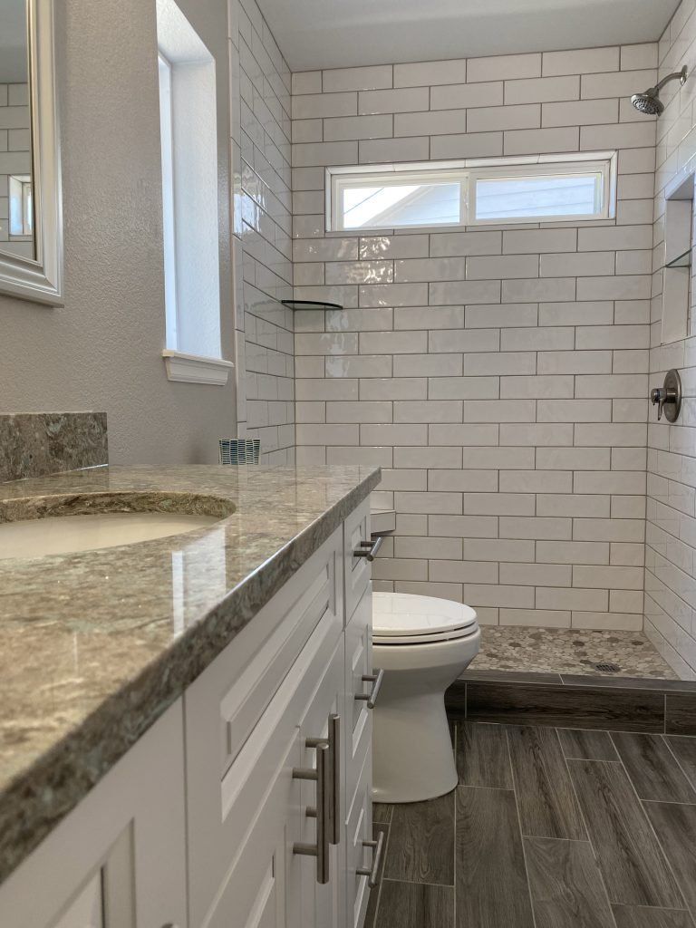 Bathroom with white subway tile shower, granite vanity, and gray wood-look floor.