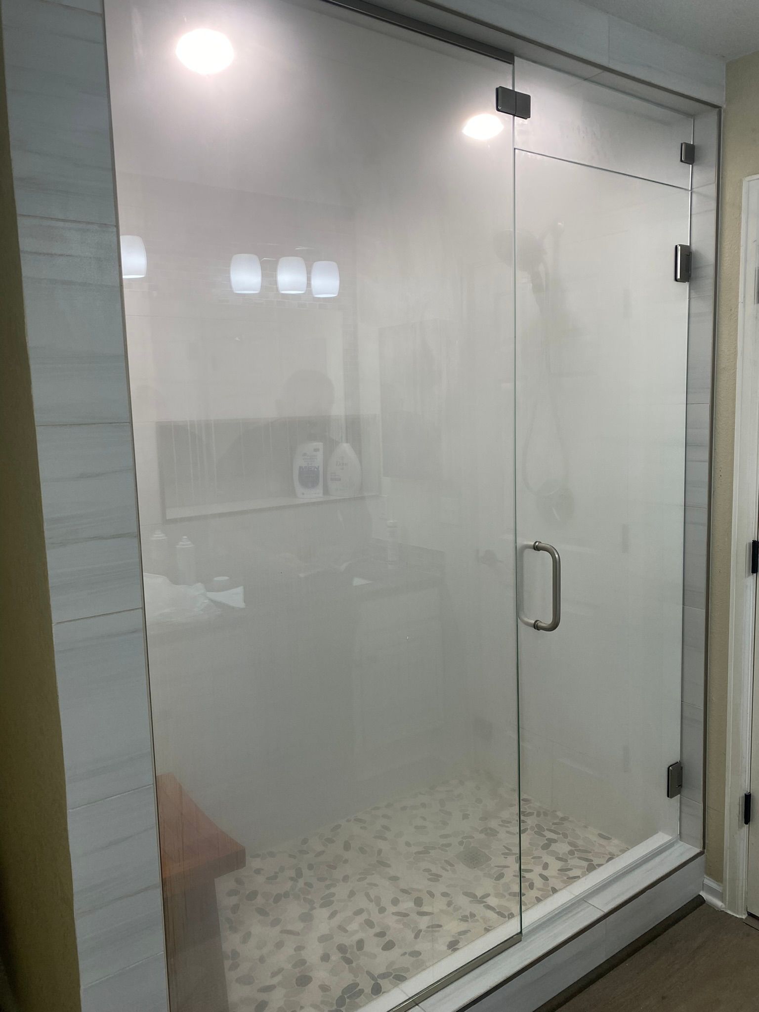 Glass shower enclosure with frosted glass door, white tile walls, and pebble-tiled floor.
