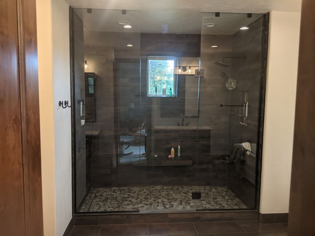 Glass shower enclosure in a bathroom with pebble floor, gray tile, and wood cabinets.