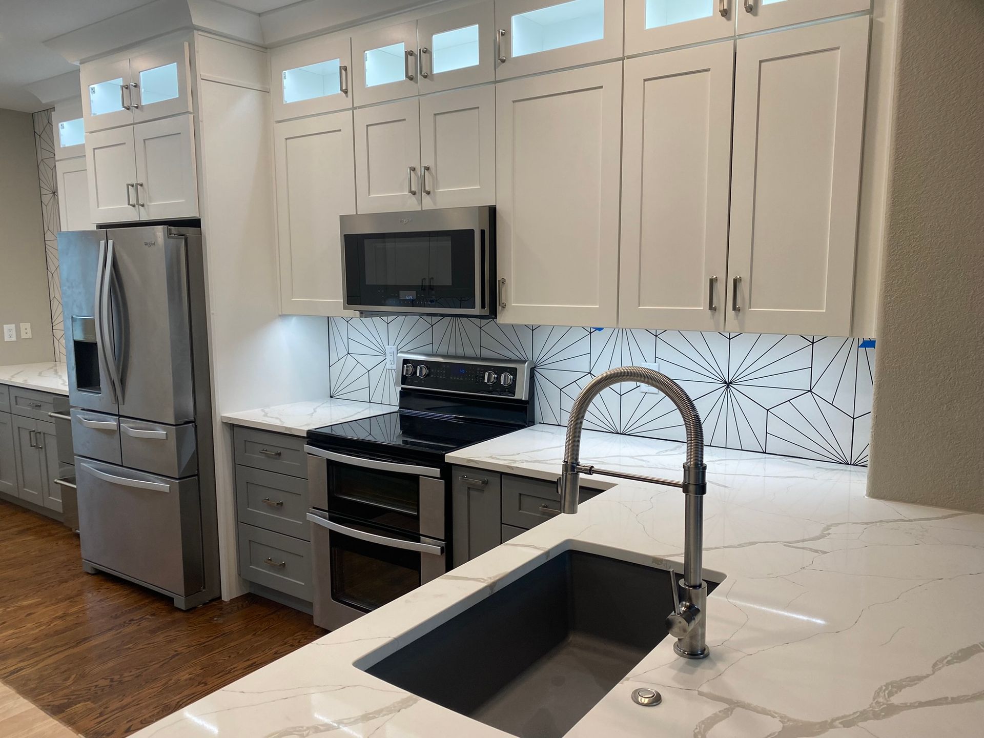 Modern kitchen with gray and white cabinets, stainless steel appliances, and white countertops.