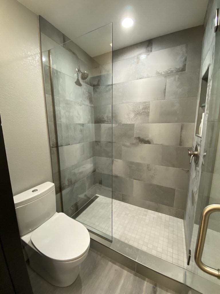 Modern bathroom with gray tiled shower and toilet. Glass shower door and chrome fixtures.
