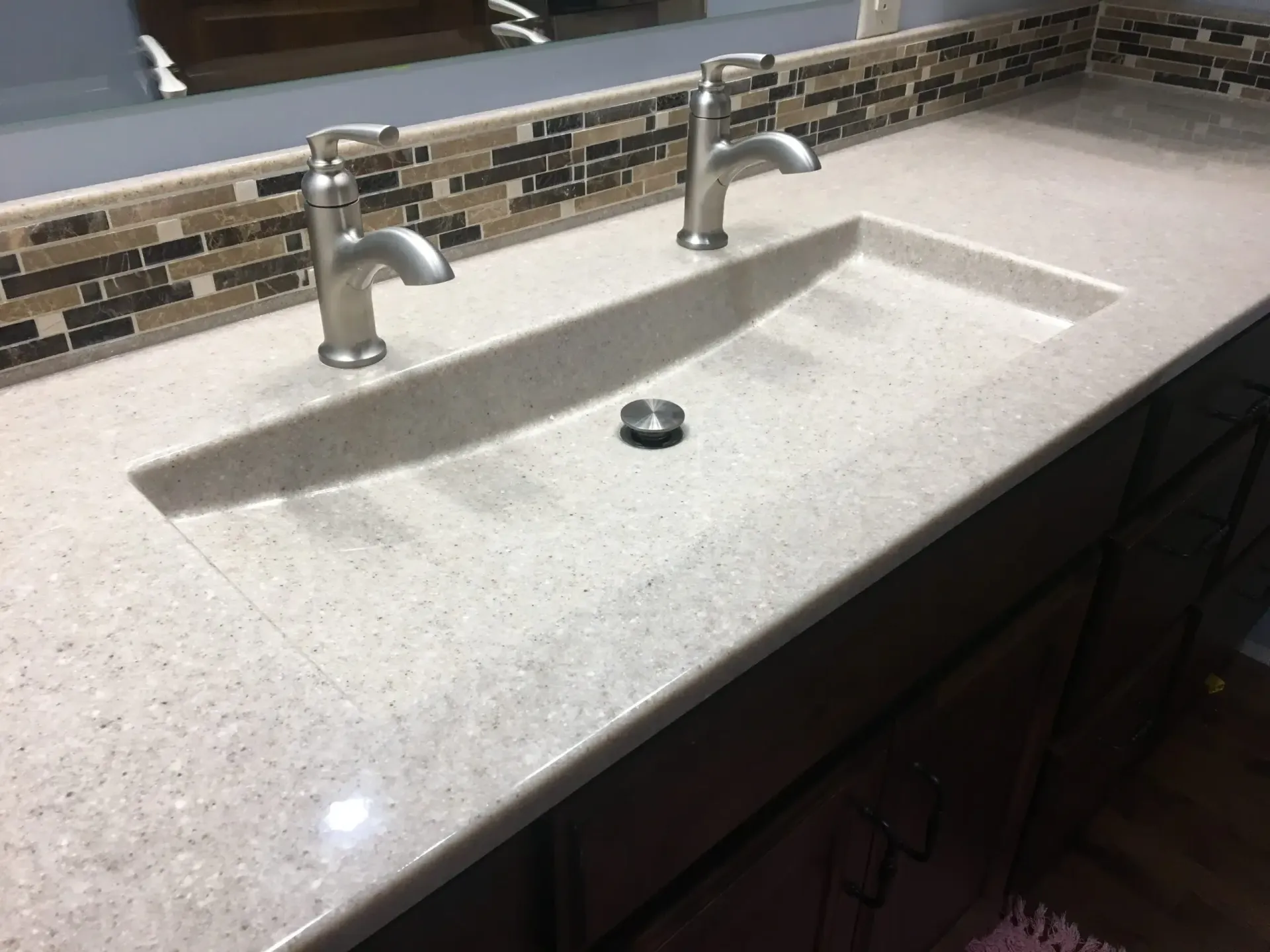 Bathroom vanity with integrated rectangular sink and two brushed nickel faucets.