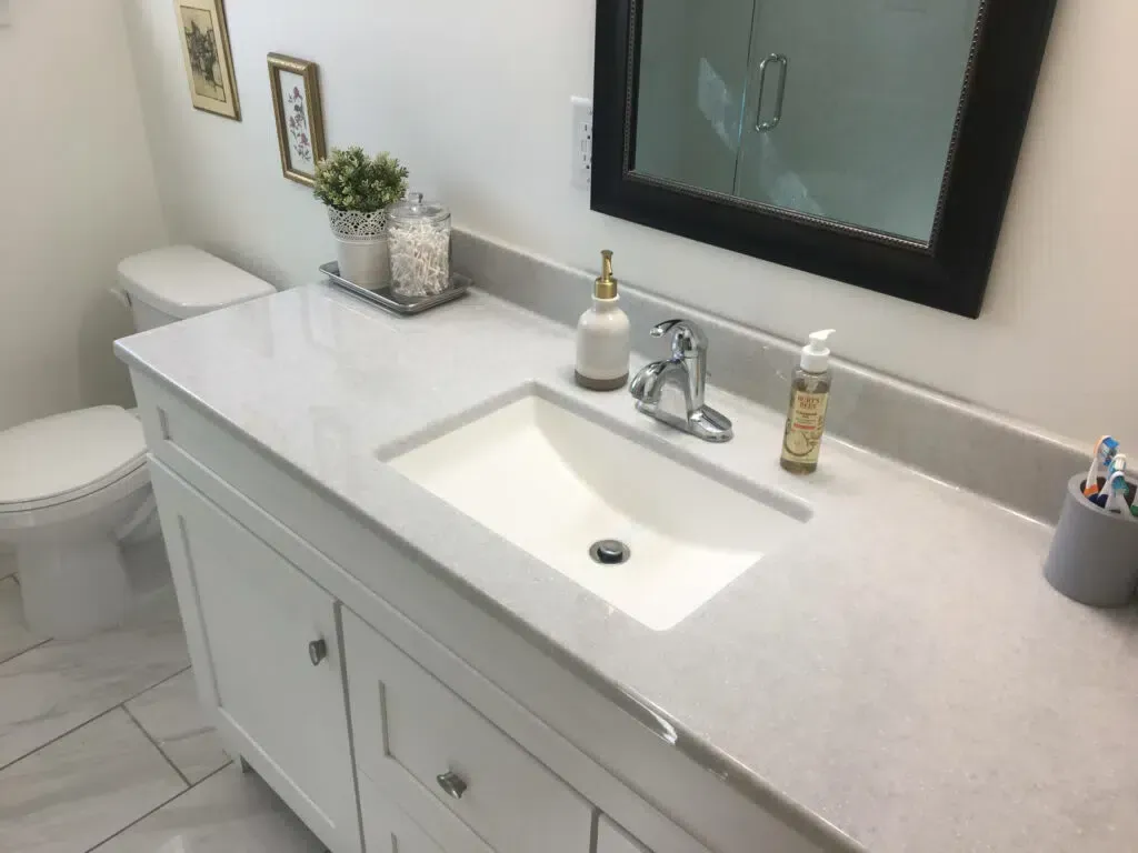 White bathroom vanity with sink, countertop, and mirror; toilet and decorative items.