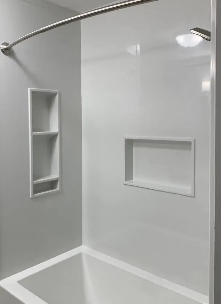 White and gray shower with built-in shelves, a curved shower rod, and a recessed light.