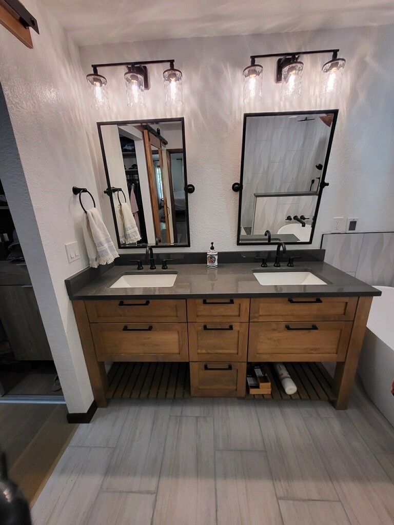 Bathroom with dual sinks, mirrors, and wooden vanity. Black fixtures, neutral colors, and tiled floor.