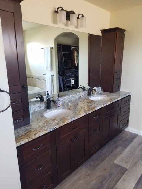Bathroom with dark brown cabinets, granite countertop, and dual sinks with a mirror.
