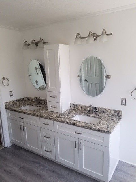 Bathroom with double sinks, white cabinets, granite countertop, oval mirrors, and wall-mounted lights.