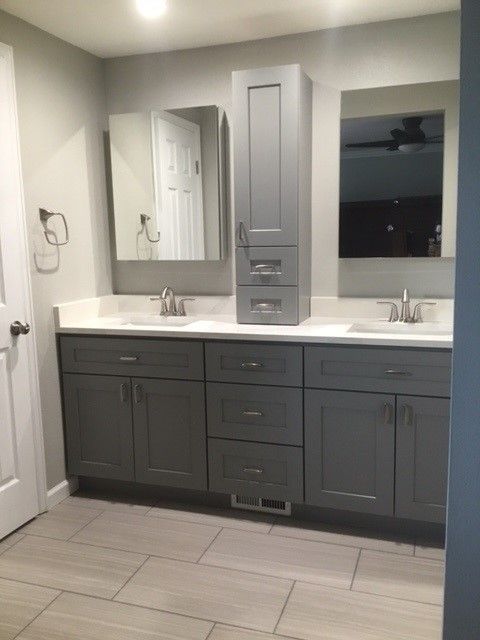 Gray bathroom with a double vanity, tall storage cabinet, mirrors, and light-colored tile flooring.