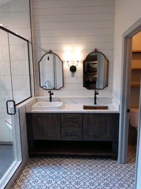 Bathroom with dark wood vanity, white countertop, two black framed mirrors, and patterned floor tile.
