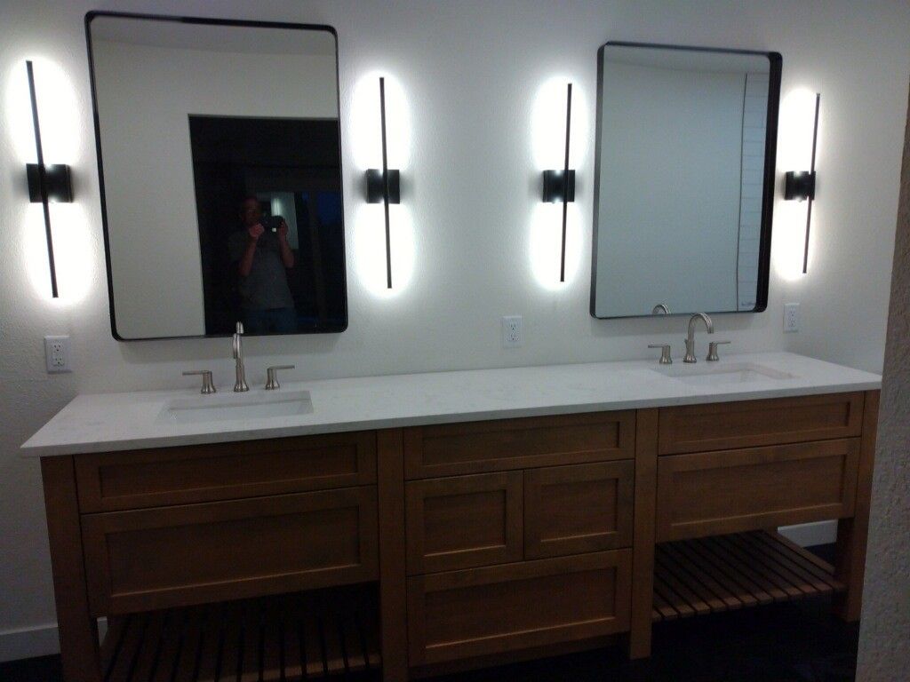 Bathroom with two mirrors, sinks, and sconce lighting above a wooden vanity.