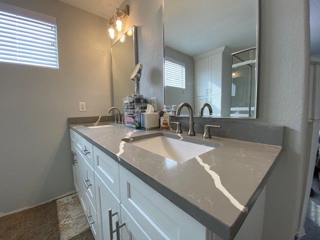Gray countertop with double sinks, white cabinets, and a large mirror in a modern bathroom.