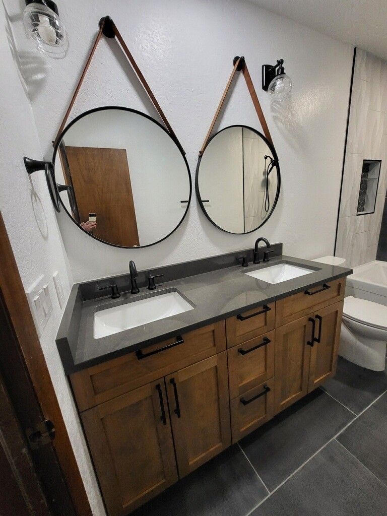 Bathroom with wooden vanity, dark countertop, round mirrors, and black hardware.