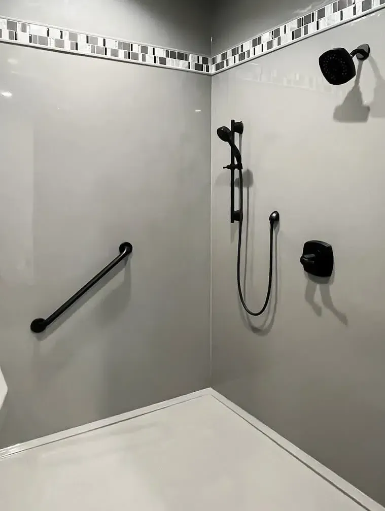 Gray shower stall with black fixtures and grab bar.