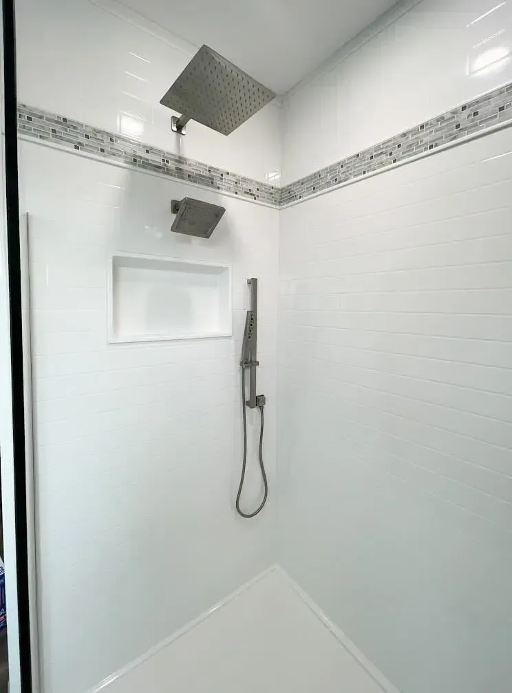 White tiled shower with two shower heads, a hand shower, and a small recessed shelf.