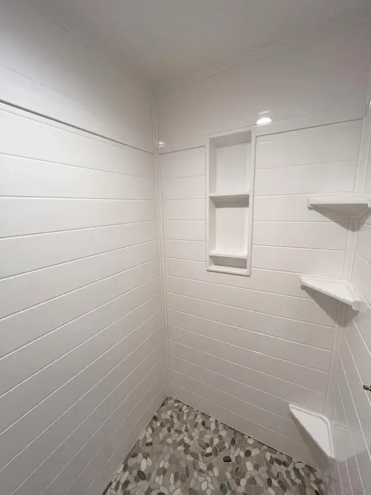 White tiled shower with stone floor and built-in shelving.