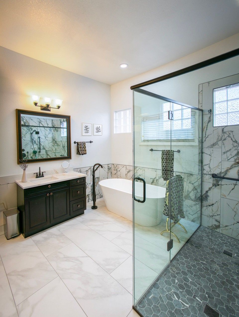Luxurious modern bathroom with marble tile, glass shower, freestanding tub, and dark vanity.