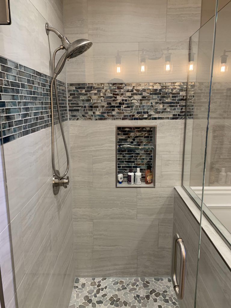 Modern shower with gray tiled walls, pebble floor, glass enclosure, and built-in niche.