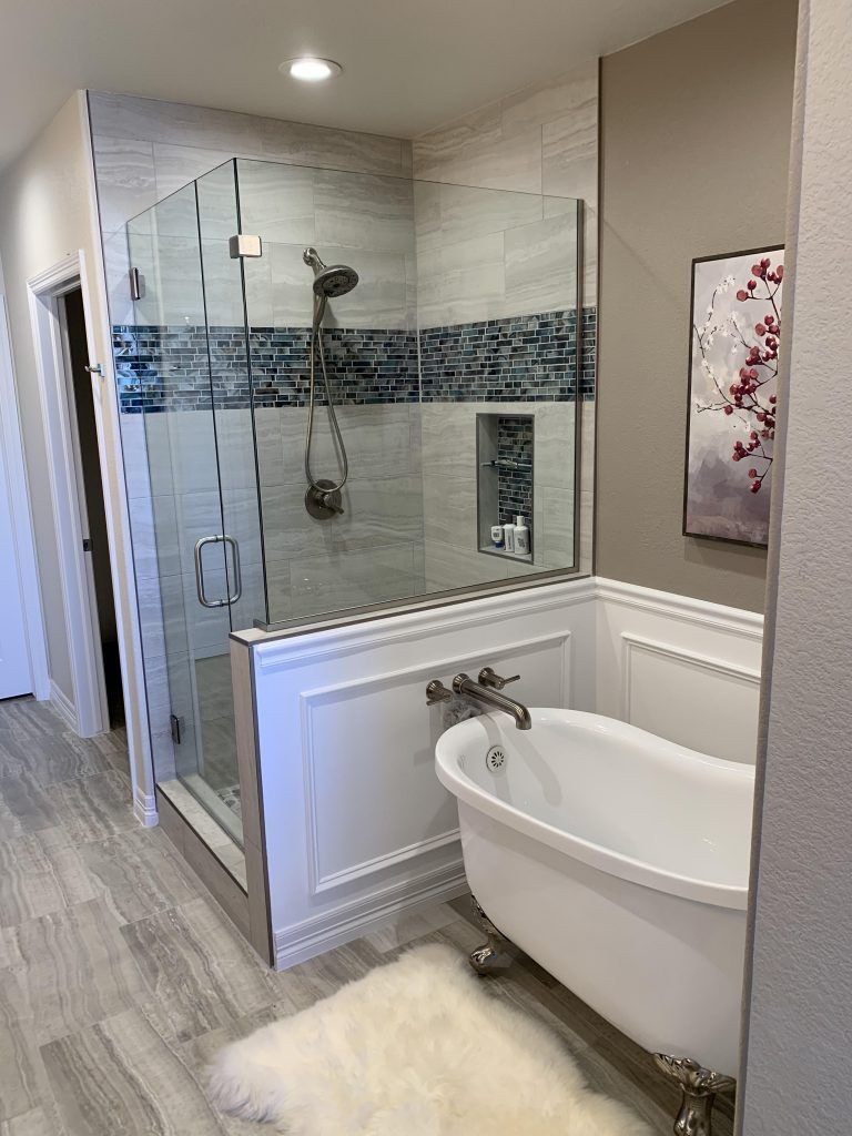 Modern bathroom with a glass shower, white tub, and artwork on a beige wall.