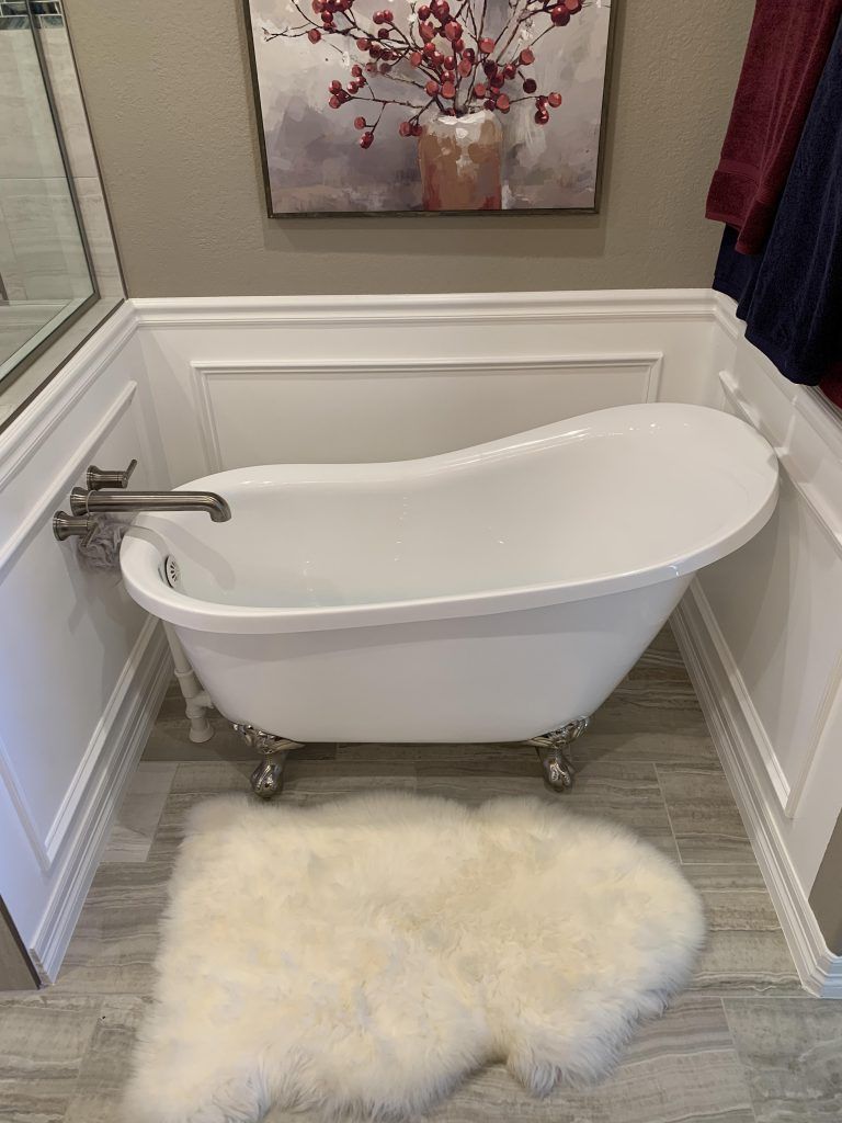 White clawfoot bathtub in a bathroom with a rug, painting, and paneling.