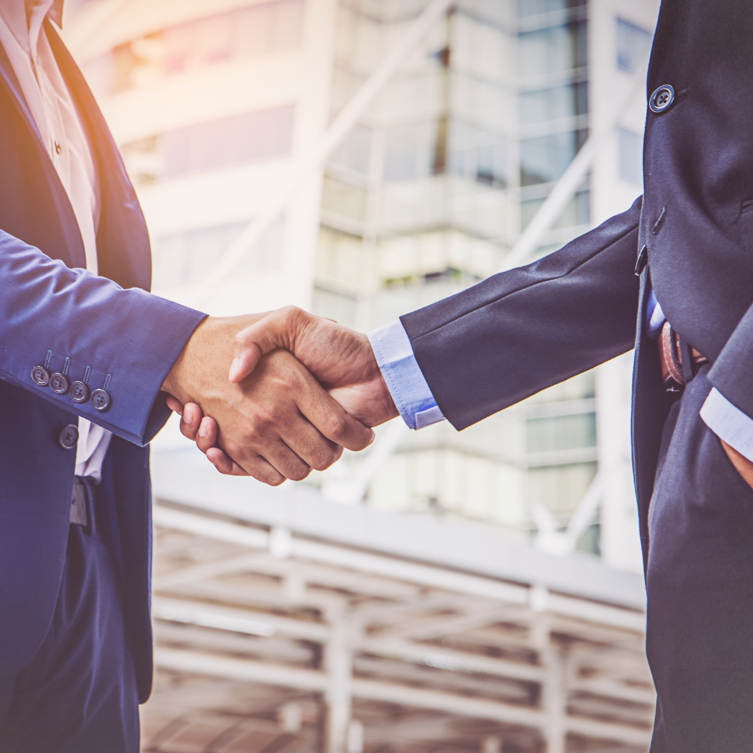 Two men in suits are shaking hands in front of a building.