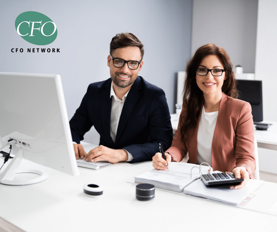 A man and a woman are sitting at a desk in front of a computer working on a financial analysis.