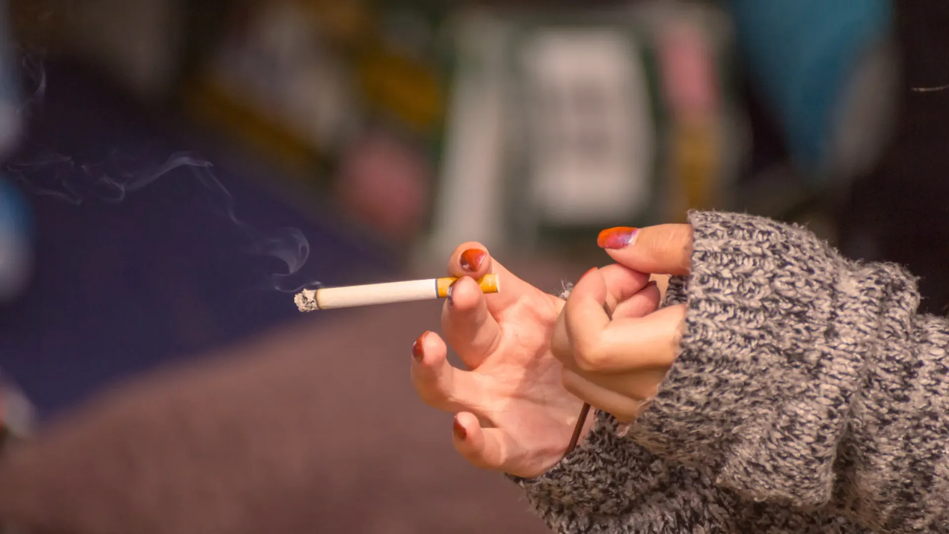 Woman holding a smoking cigarette while indoors.